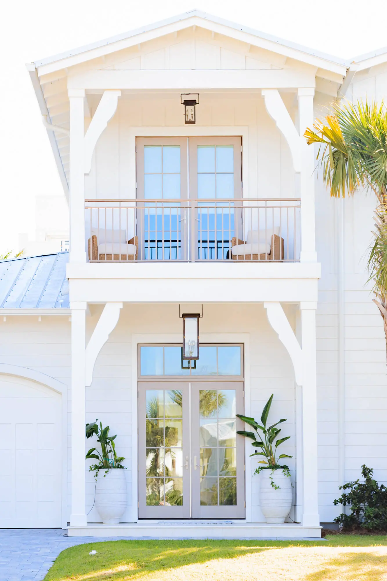 A bright, white two-story coastal home featuring tan French doors and a second-floor balcony, showcasing a premium exterior finish by Grayton Painting.