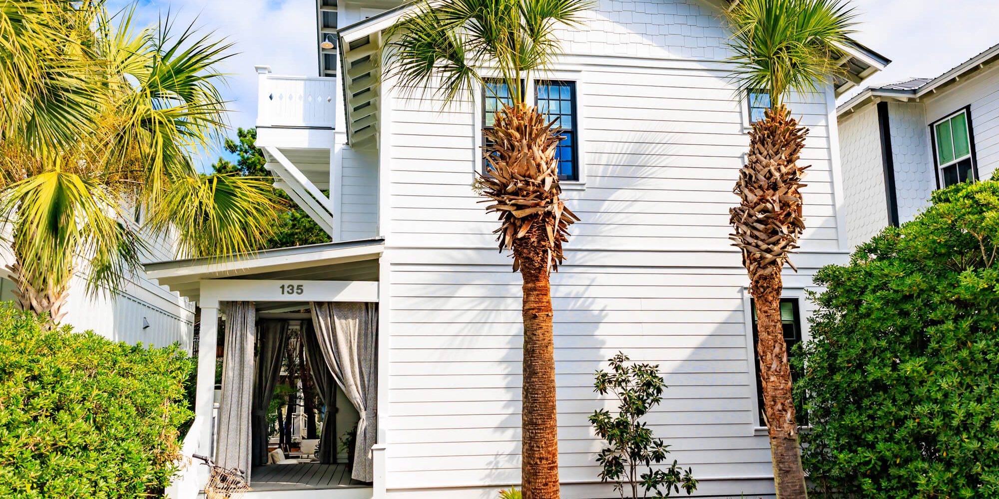 A bright, coastal white two-story home with crisp exterior finishes and palm tree landscaping, expertly completed by Grayton Painting.