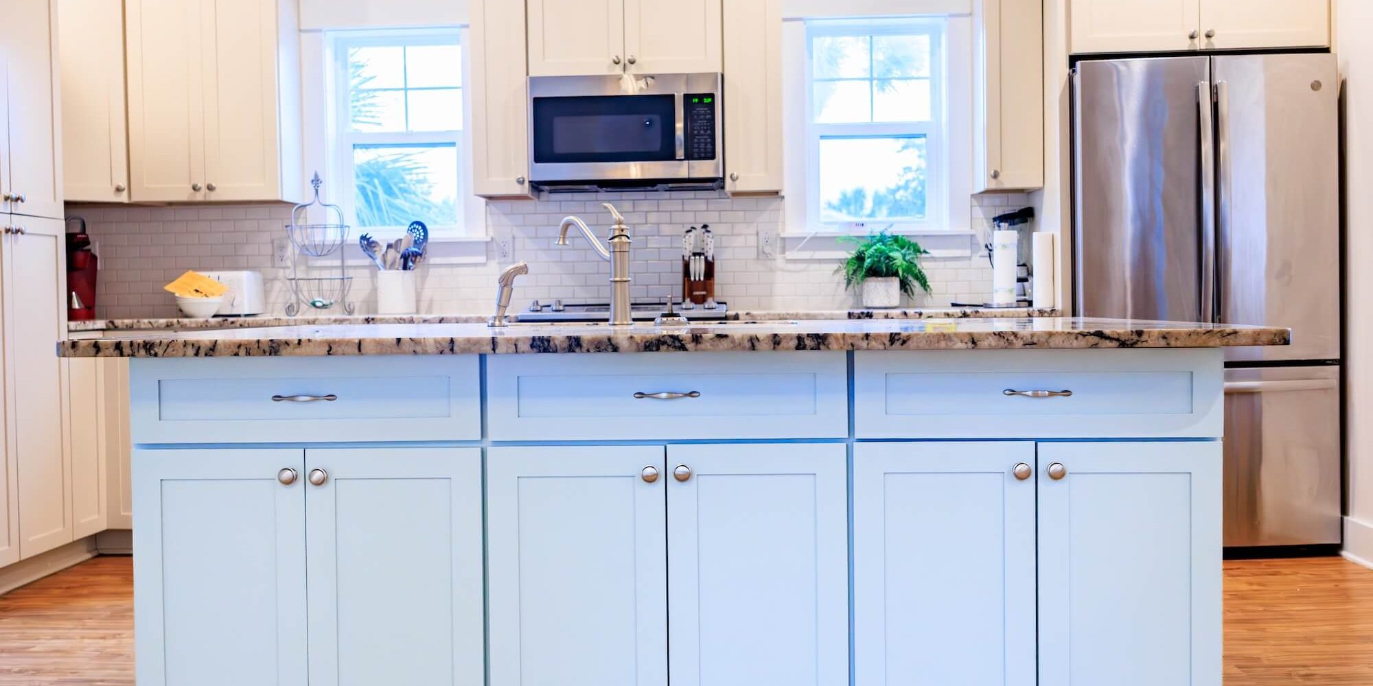A modern kitchen featuring custom-painted light blue island cabinetry and off-white perimeter cupboards, showcasing the high-end cabinetry finishes provided by Grayton Painting.